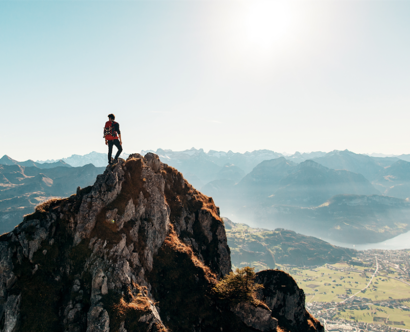 Rock climber standing at the top of a mountain, overlooking the valley below