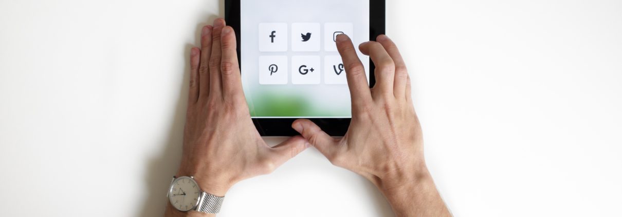 Person holding tablet with icons of social media platforms on the screen