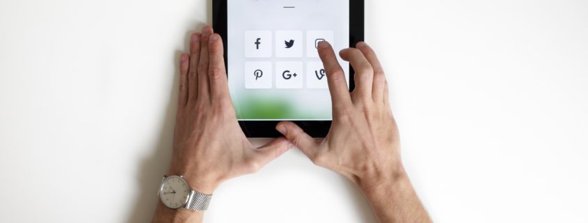 Person holding tablet with icons of social media platforms on the screen